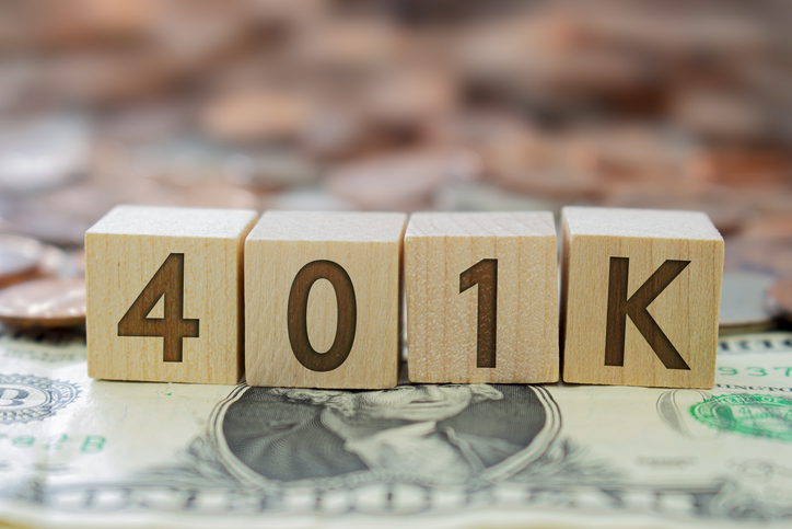 A wooden block displaying “401K” surrounded by cash, symbolizing retirement planning in the United States.
