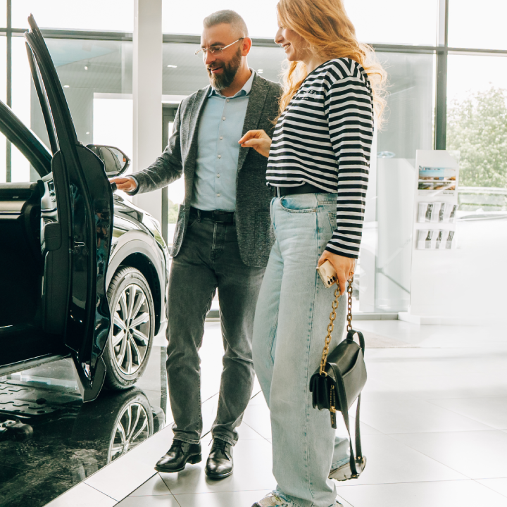 Car salesman showing a new car to a customer in a dealership.