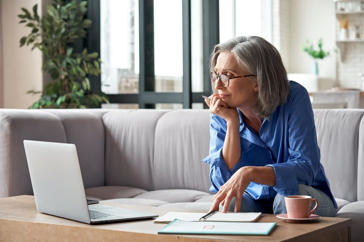 Older woman working on papers and laptop. Taxes and budget.