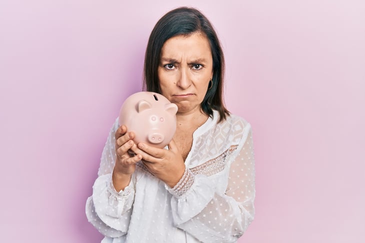 Unhappy middle-aged woman holding a piggy bank.